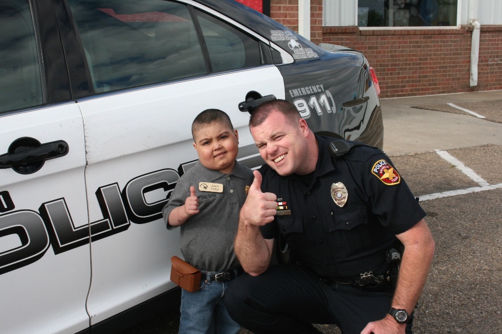 Jace and a police officer standing next a police car. They are giving a thumbs-up.